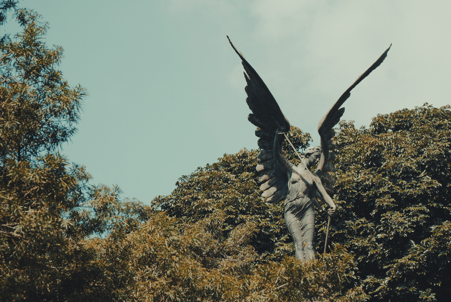 A statue shooting an arrow protruding out the top of a few trees