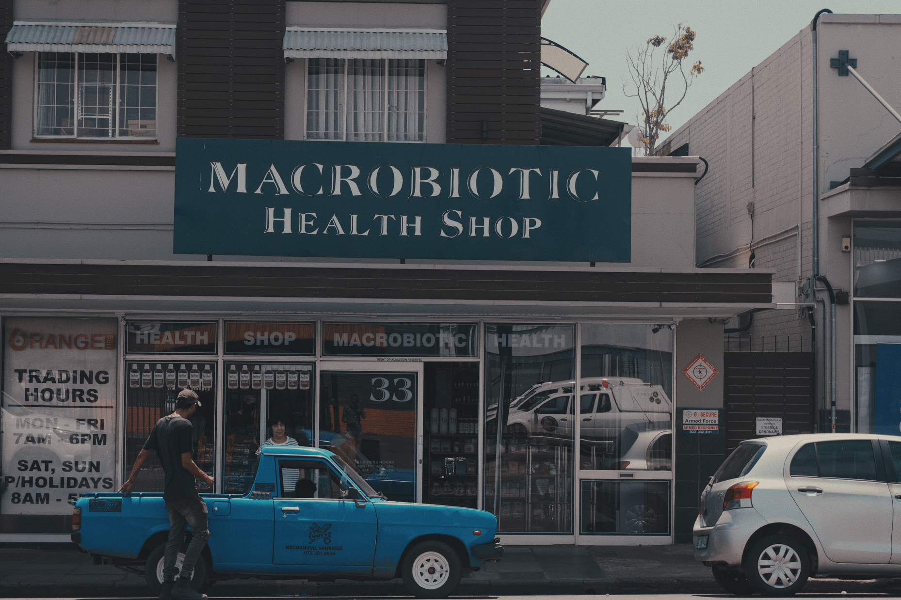 A macrobiotic store in the background of a man getting into his blue lorry